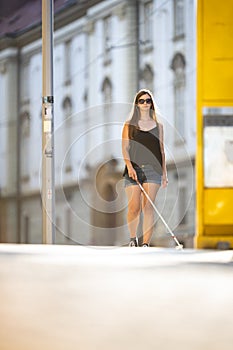 Blind woman walking on city streets, using her white cane