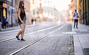 Blind woman walking on city streets, using her white cane