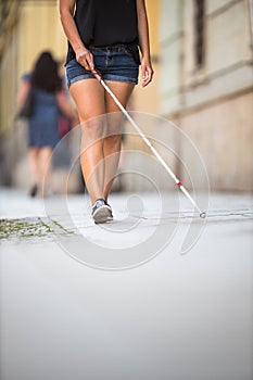 Blind woman walking on city streets, using her white cane