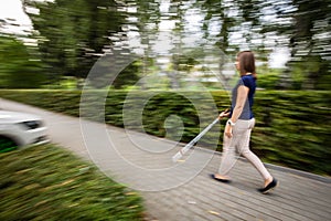 Blind woman walking on city streets, using her white cane