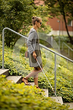 Blind woman walking on city streets, using her white cane