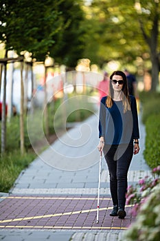 Blind woman walking on city streets, using her white cane