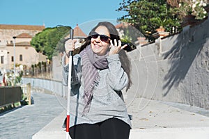 Blind woman with a white cane using a smartphone to listen some messages. Visually impaired concept with empty copy space.