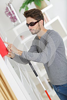 Blind young man with stick and dark glasses at home