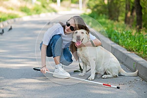 Blind young woman cuddling with guide dog on a walk outdoors.