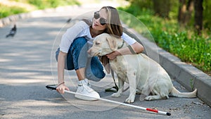 Blind young woman cuddling with guide dog on a walk outdoors.