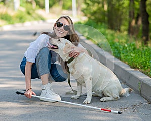 Blind young woman cuddling with guide dog on a walk outdoors.