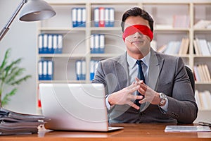 The blindfold businessman sitting at desk in office