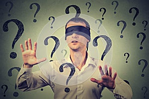 Blindfolded man stretching his arms out walking through many question marks