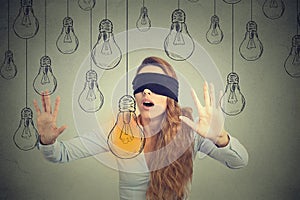 Blindfolded woman walking through light bulbs searching for bright idea