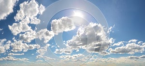 Blinding sun piercing through cloud bank from blue sky, panorama