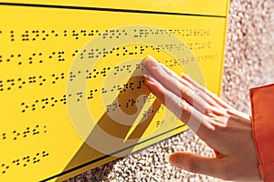 Blindness. A woman reads a yellow Braille sign. Close up of hands. Concept of the day of the blind and disability