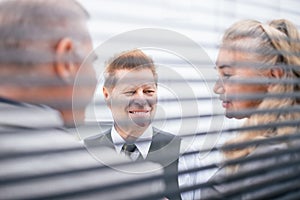 Through the blinds. business colleagues talking standing in the office.