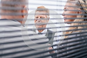 Through the blinds. business colleagues talking standing in the office.