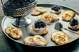 Blinis with black caviar, on a festive dish on a black background, mini pancakes