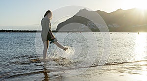 Bliss Teenager splashing while kick the water with the leg, having fun in the sea walking in the sunset. Lady laugh and splash