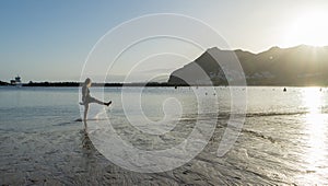 Bliss Teenager splashing while kick the water with the leg, having fun in the sea walking in the sunset. Lady laugh and splash