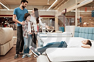 Blissful family buys new orthopedic mattress in furniture store. Happy family choosing mattresses in store.