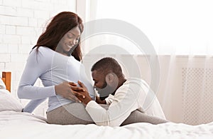 Blissful man kissing his happy pregnant wife belly