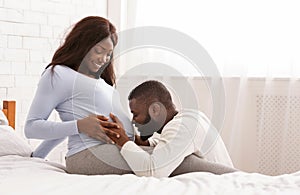 Blissful man kissing his happy pregnant wife belly photo