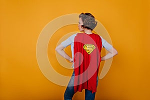 Blissful slim girl with short haircut standing in studio in superhero cloak. Photo of curly shapely woman in carnival