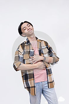 A blissful young asian man rubbing his stomach feeling satiated and full. Isolated on a white background