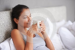 Blissfully day dreaming away. a beautiful young woman daydreaming in bed with her morning coffee.