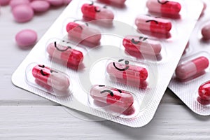 Blister of antidepressants with different emoticons on white wooden table, closeup