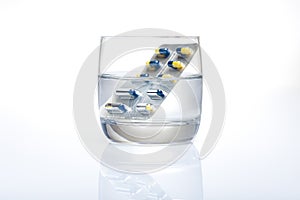 Blister of blue and yellow pills in a glass of water