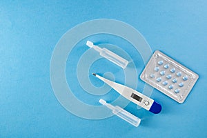 Blister pack of blue pills, ampoules and thermometer on blue background