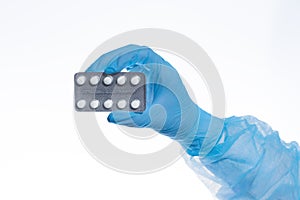 A blister of pills in a doctor`s hand, a hand in a medical glove holds a pack of pills on a white background isolate