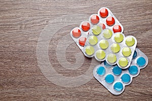 Blisters with colorful cough drops on wooden background, flat lay. Space for text