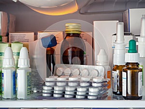 Blisters with pills, bottles with drops, sprays and gels, as well as boxes with drugs close-up on the refrigerator shelf.