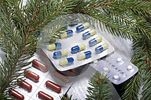The blisters with pills. Different colors. Spruce and pine branches with cones. On a wooden box