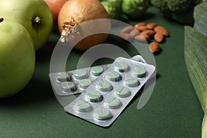 Blisters with pills and food on green background, closeup. Prebiotic supplements