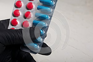 Blisters with red and blue tablets in hand in a rubber glove. On a light background. Close-up