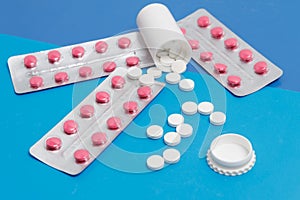 Blisters rose capsule and white round tablets on blue background, medical pharmacy concept