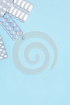 Blisters of white and blue pills on blue background, top view. Different pharmaceuticals, tablets, medicine capsules.