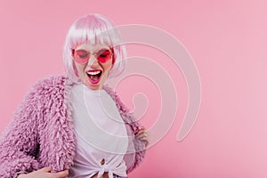 Blithesome girl in periwig dancing on pink background. Excited young woman in peruke expressing hap