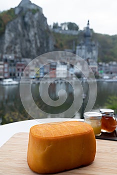 Block of Belgian abbey cheese made with brown trappist beer and view on Maas river in Dinant, Wallonia, Belgium