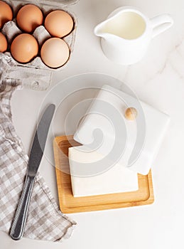 Block of butter in butter dish with milk and eggs on a marble background.