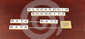 Block chain security spelled out in tiles on a cherry wood background with data and a processor chip underneath