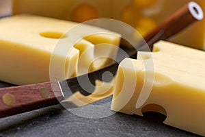 Block of Swiss medium-hard yellow cheese emmental or emmentaler with round holes and cheese knife