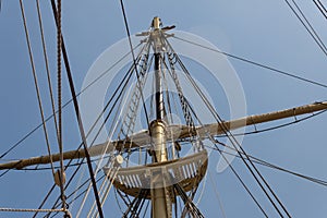 Block and tackle, rigging, and shrouds surrounding a mast on a vintage tall ship, blue sky, marine theme