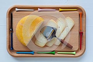 Block of tasty cheese on cutting board with a knife and golf tee