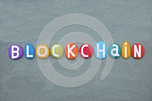 Blockchain, creative text composed with multi colored stone letters over green sand