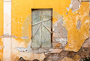 Blocked old wooden window, on yellow painted weathered wall.