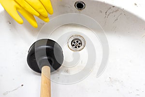 Blocked sewer, clogged wash bowl, basin drain, yellow rubber gloves and a plunger near in the bathroom at home