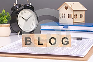 blog word in wooden blocks with small wooden house and alarm clock on gray background. timely and home-oriented approach