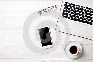 Blogger / businessman / businesswoman, it specialist`s white wood office space table with laptop, blank screen smartphone, coffee